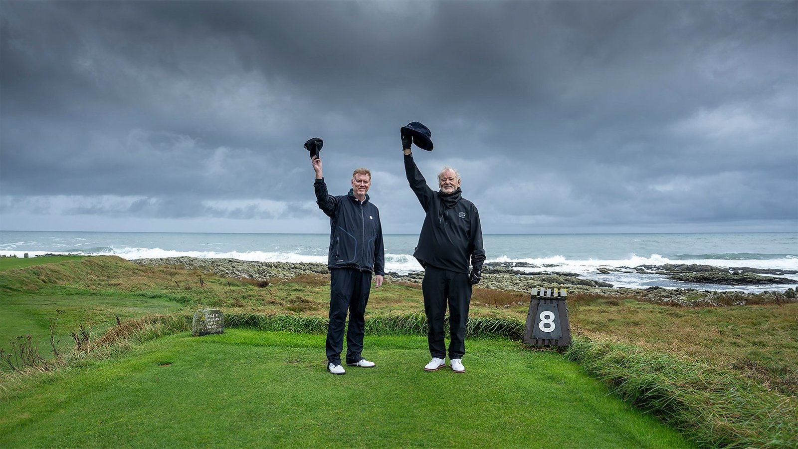 A Course Called Ireland resmi karesinden deniz kenarındaki golf sahasında şapkalarını havaya kaldıran Tom Coyne ve Bill Murray