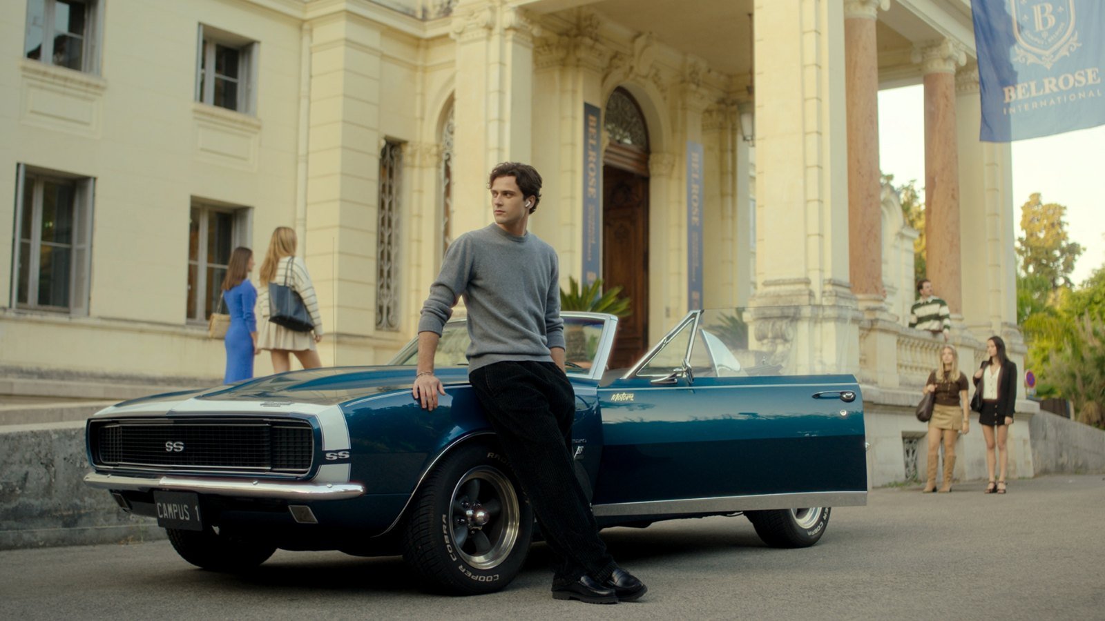 Campus Drivers 6 Kasım’da Prime Video’da: C.S. Quill’in çok satan üniversite romantizmi Fransız dizisi oluyor 2026 – 2 Campus Drivers resmi karesinde görkemli bir üniversite binasının önünde üstü açık klasik bir arabaya yaslanmış gri kazaklı genç adam