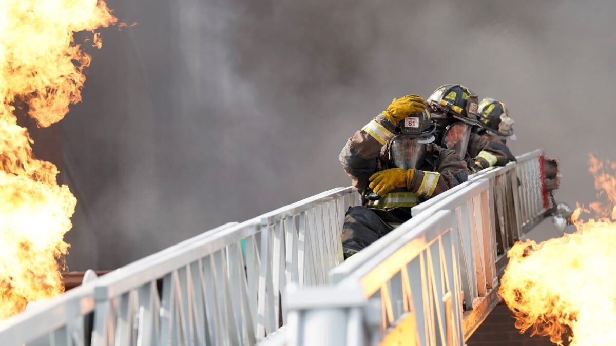 Chicago Fire 15. sezon NBC resmi karesinden Leroy Williams III ve David Eigenberg alevler arasında merdivende