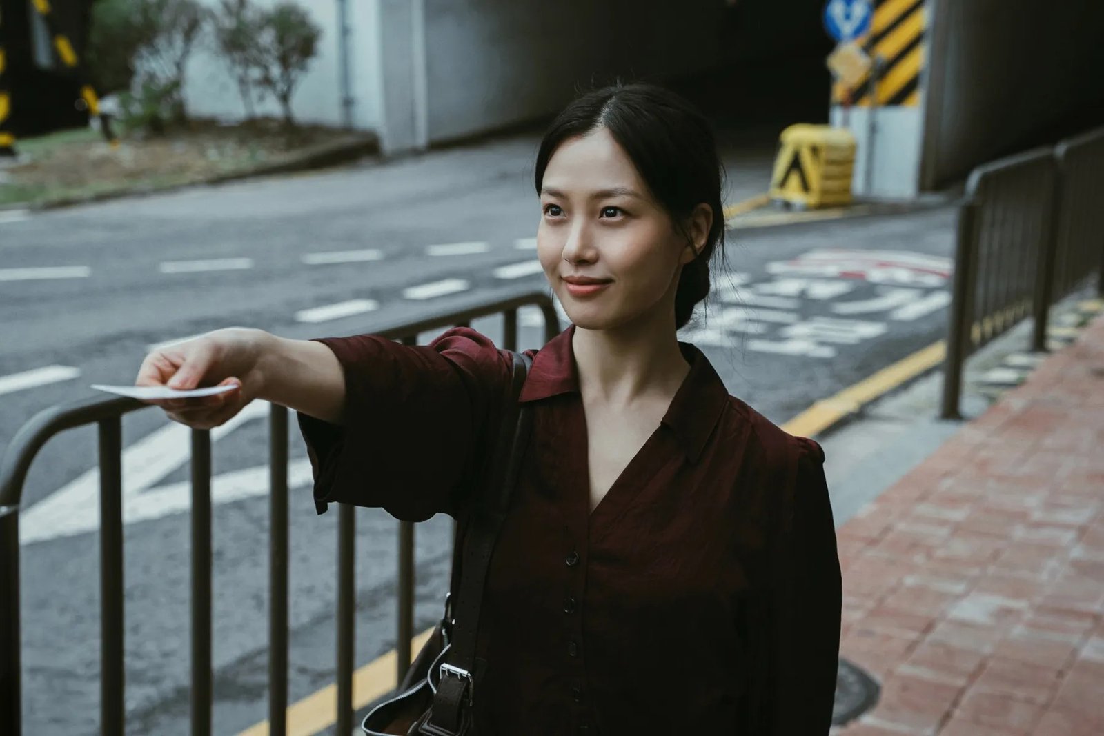 Dead-End Job 30 Ekim’de Netflix’te: Lee Jae-wook’lu Kore dizisinde ölümcül yarı zamanlı iş 2026 – 2 Dead-End Job Netflix resmi karesinden bir sokakta korkuluğun yanında elindeki kartı uzatan genç bir kadın