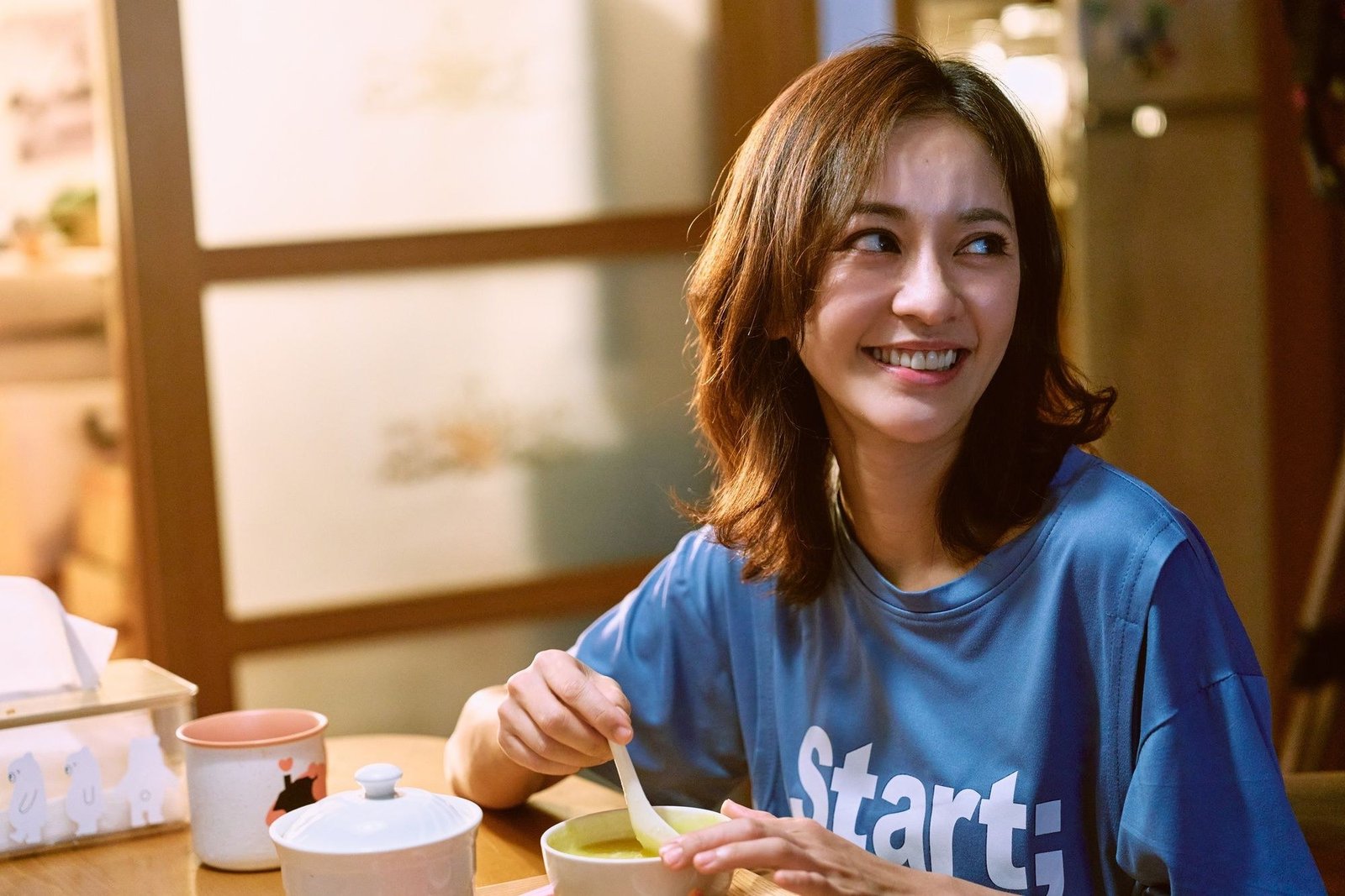 Driving Mom Crazy resmi karesinden mavi tişörtle masada yemek yerken gülümseyen Ivy Chen