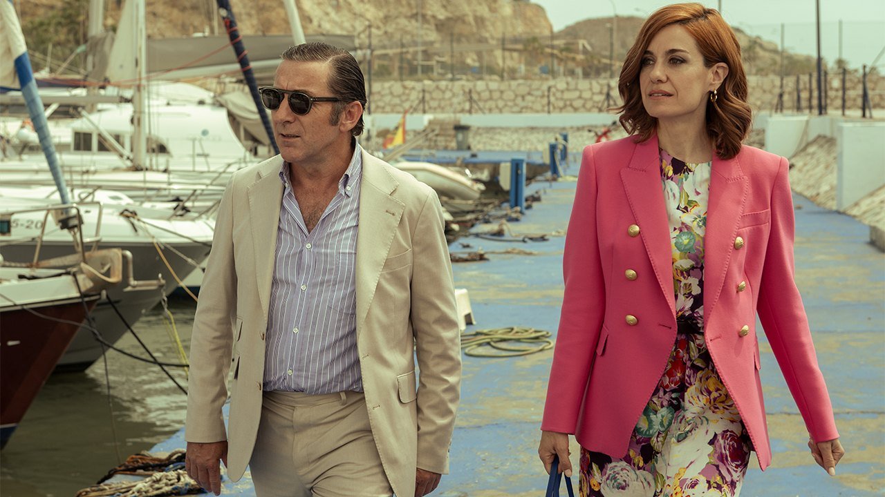 Fading Grandeur Netflix resmi karesinden bir marinada yürüyen Antonio de la Torre ve pembe ceketli Alexandra Jiménez