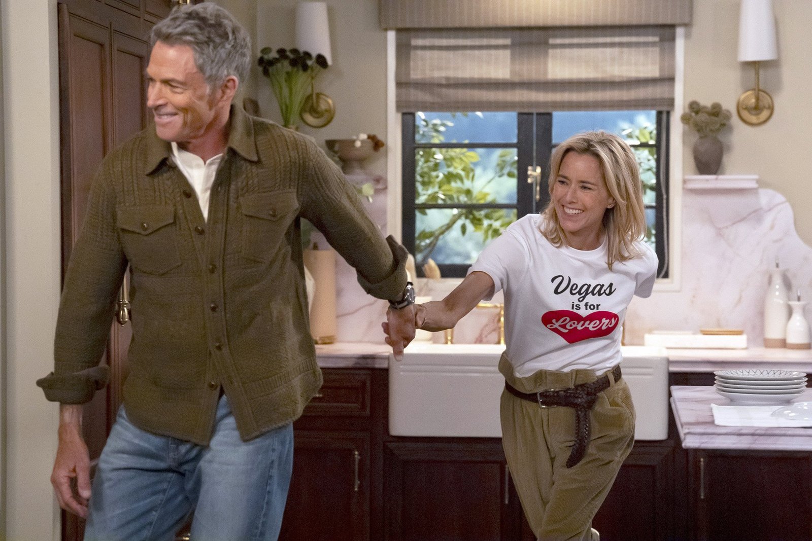 Newlyweds NBC resmi karesinden mutfakta el ele tutuşan James rolündeki Tim Daly ve Jeanie rolündeki Téa Leoni