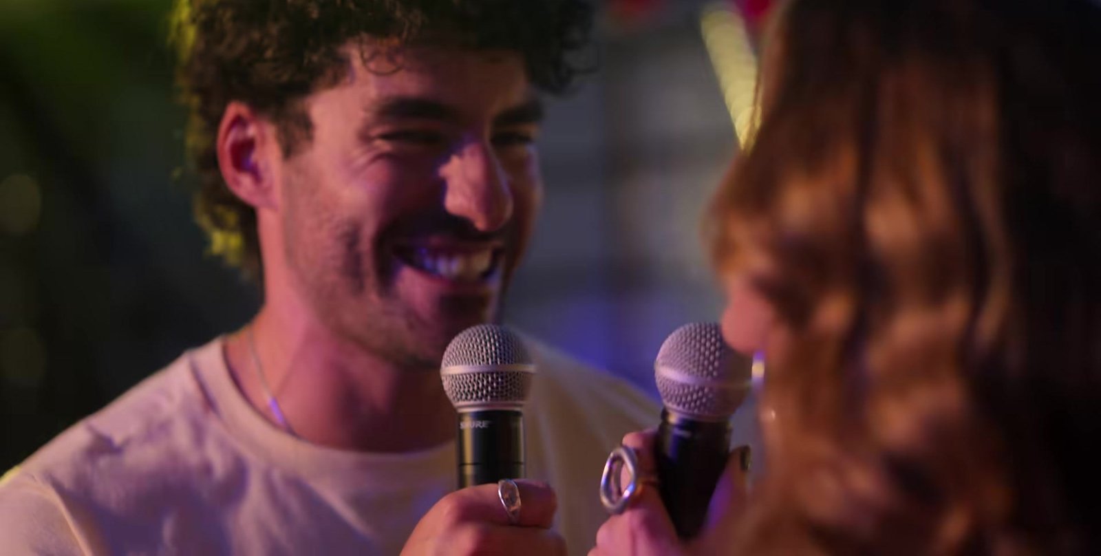 Os 12 Signos de Valentina fragmanından mikrofonla karaoke yapan kıvırcık saçlı genç adam ve karşısındaki kadın