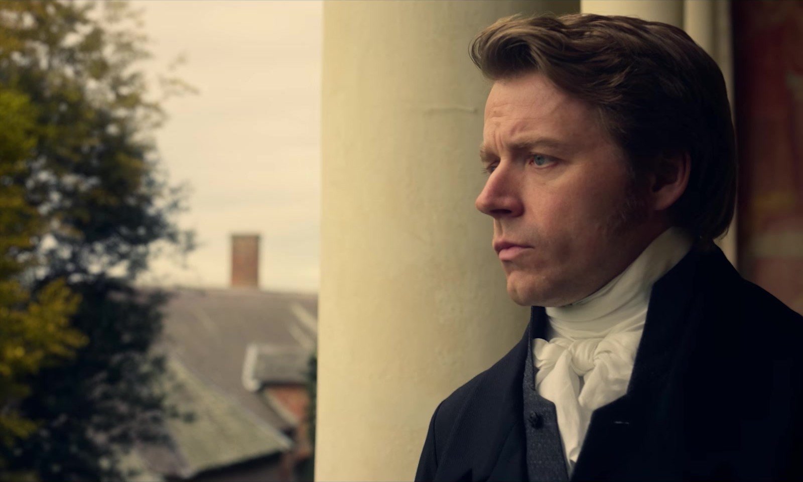 Pride and Prejudice fragmanından beyaz fuları ve koyu ceketiyle düşünceli bakan dönem kıyafetli bir beyefendi