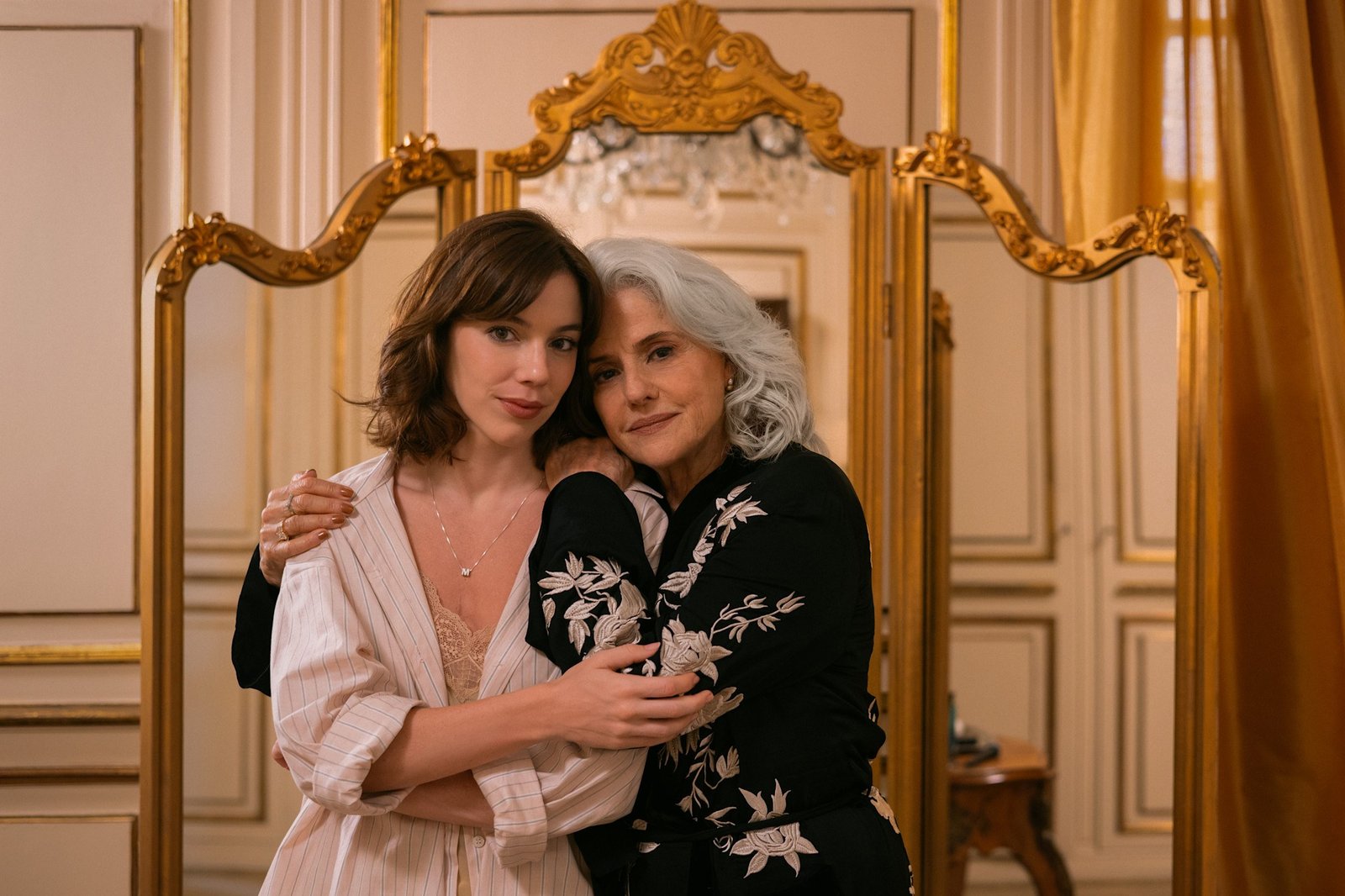 The Gift of Deceit Netflix resmi karesinden yaldızlı bir aynanın önünde sarılan Maíra Rossetti rolündeki Alice Wegmann ve Lúcia Rossetti rolündeki Marieta Severo