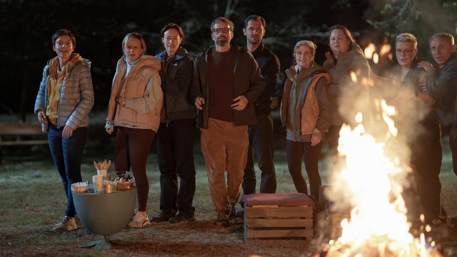 The Mothers of Penguins 2. sezon resmi karesinden gece yanan bir ateşin etrafında toplanmış yetişkinler ve çocuklar
