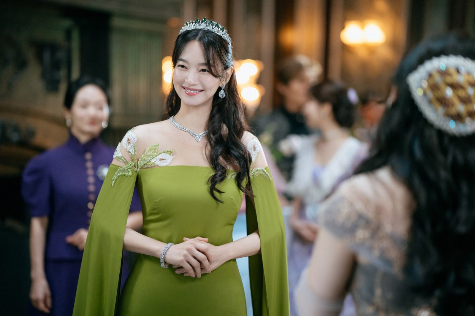 The Remarried Empress resmi karesinde yeşil pelerinli elbise ve tacıyla saray davetinde gülümseyen İmparatoriçe Navier rolündeki Shin Min Ah