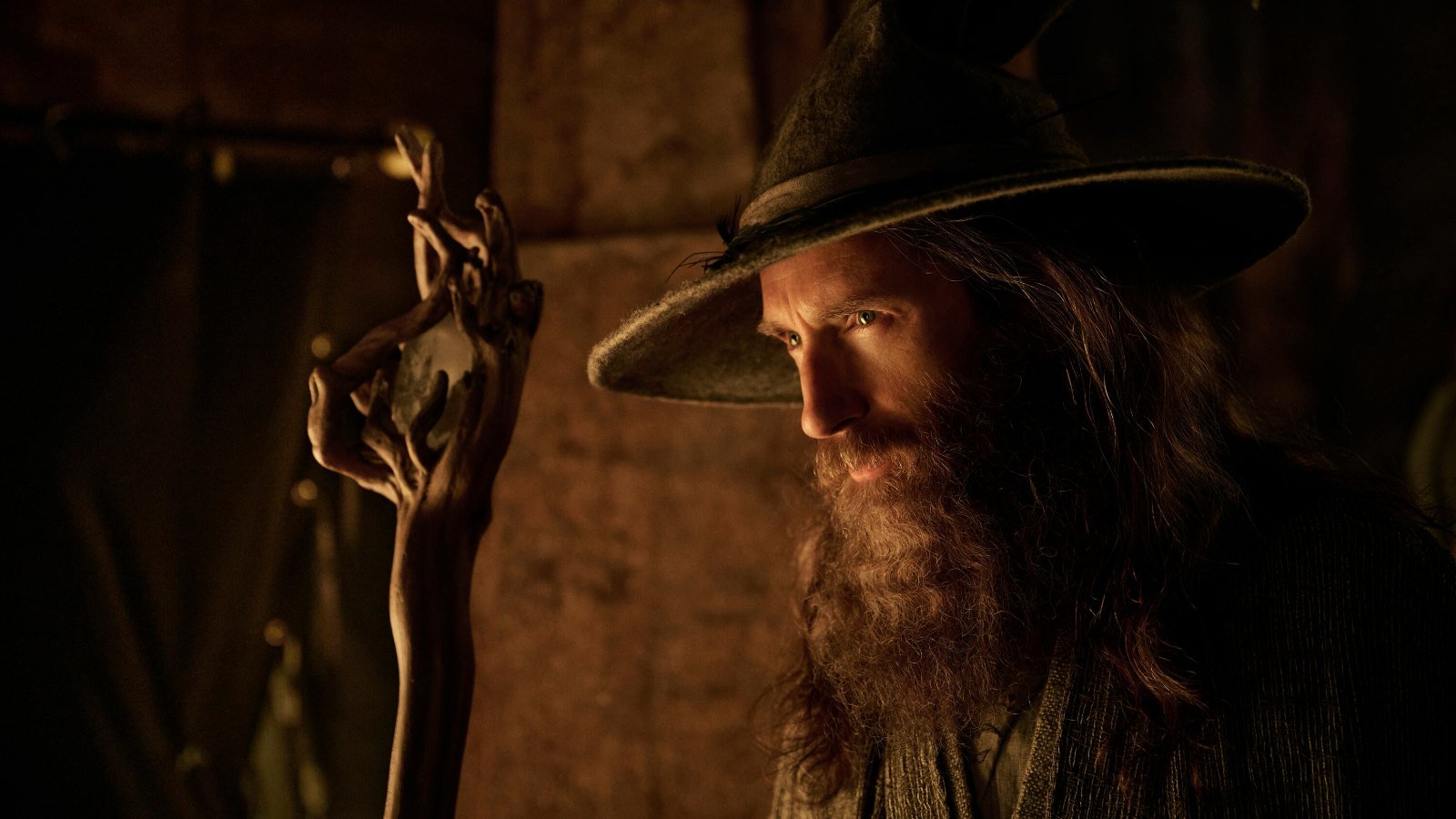 Güç Yüzükleri 3. sezon 11 Kasım’da Prime Video’da: Sauron Tek Yüzük’ün peşinde, Celeborn sonunda sahnede 2026 – 2 Güç Yüzükleri üçüncü sezonundan resmi karede geniş kenarlı şapkası ve uzun sakalıyla karanlıkta asasına dayanan Gandalf rolündeki Daniel Weyman